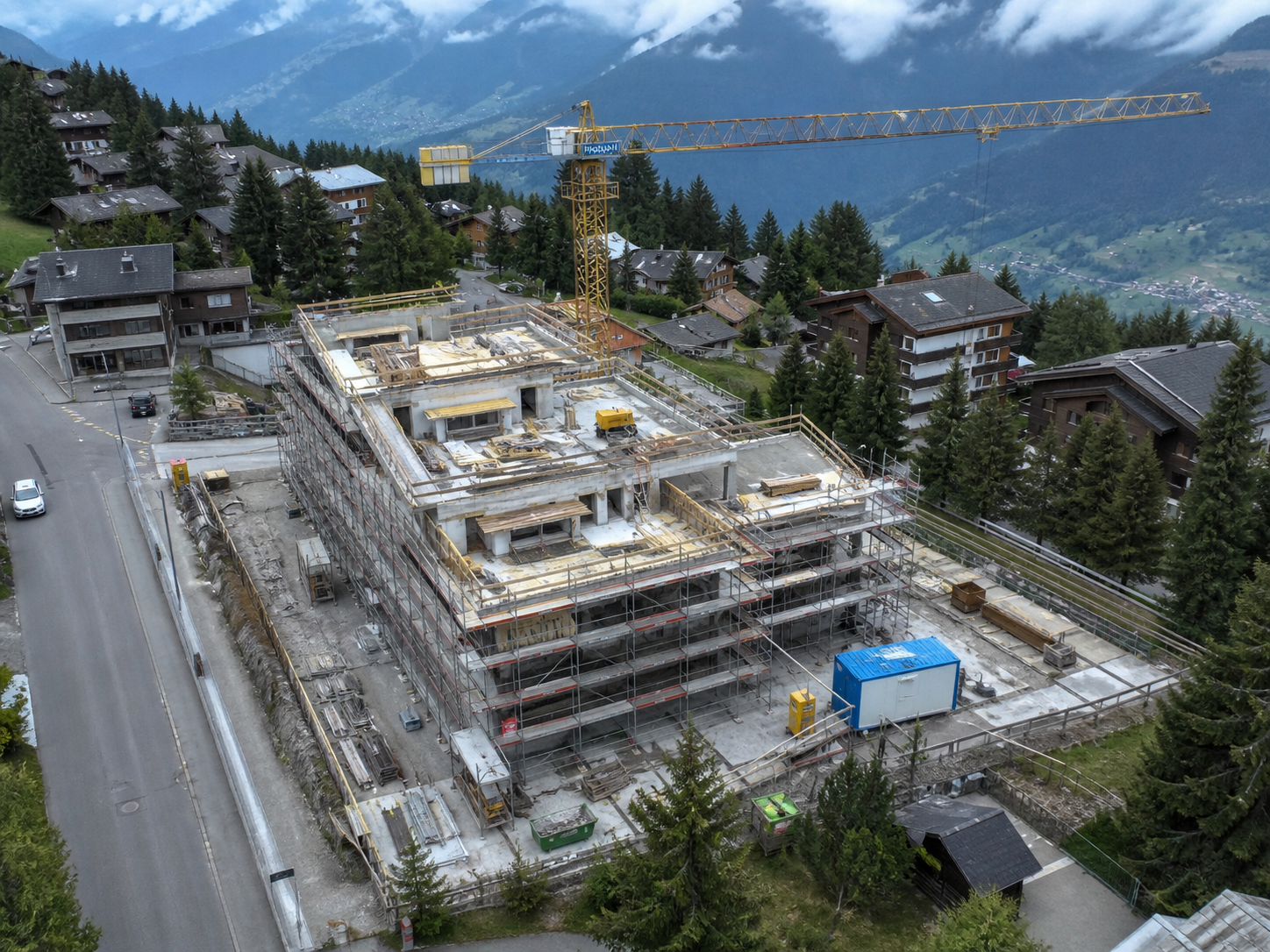Mountain construction site with a tower crane, surrounded by alpine homes and
